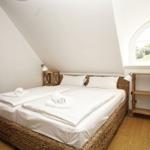 Schlafzimmer mit Doppelbett, Holzboden und zwei Fenstern.