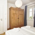 Schlafzimmer mit Holzschrank, Bett und Fenster mit Vorhängen.