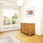 Ein Zimmer mit Holzboden, einem Schrank und einer Glastür zum Balkon.