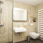 Badezimmer mit Dusche, Waschbecken und Toilette. Weiße Wandheizung und Spiegelschrank.