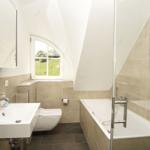 Badezimmer mit Badewanne, Toilette und Waschbecken unter einem Dachfenster.