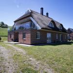 Ein zweistöckiges Haus mit Dachterrasse und Schornsteinen steht auf einer grünen Wiese.