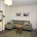Wohnzimmer mit Ecksofa, Tisch, Stehlampe und Wandbildern.