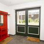Eingang mit rotem Garderobenhaus und grünen Glastüren zur Außenterrasse.