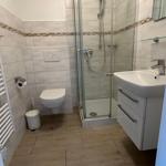 Badezimmer mit Dusche, Waschbecken und Toilette. Fliesen und Holzoptik.