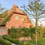Red brick house with thatched roof, surrounded by greenery and trees.