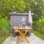 Wooden table with two chairs in front of a wooden shed in the garden.