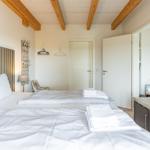 Zimmer mit Doppelbett, Holzbalkendecke und Wandbildern. Nebenraum ist sichtbar.