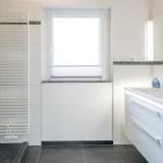 Badezimmer mit Dusche, Waschbecken und Fenster.