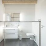 Badezimmer mit Waschbecken, Toilette und Glasdusche. Weiße Fliesen und Holzbalken.