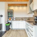 Küche mit weißen Schränken, Holzboden und Holzdecken. Links steht ein Holzofen.