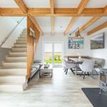 Haus mit Holzdecken, Treppe, Esstisch und Kaminofen. Blick auf grüne Landschaft.