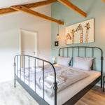 Schlafzimmer mit Bett, Wandbild und Holzbalken an der Decke.