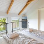 Schlafzimmer mit Doppelbett, Holzbalkendecke und Fenstern zum Balkon.
