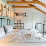 Schlafzimmer mit Doppelbett, Giraffenbild und Holzbalken an der Decke.