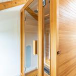 Eine Holzsauna mit Glasfront und Bedienfeld. Innere Holzwandung und Sitzbänke sichtbar.