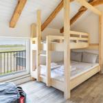 Zimmer mit Holzbett, Fenster und Sicht auf Feld
