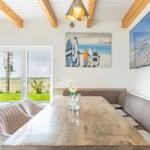 Esszimmer mit Holztisch, Sitzbank und Wandbildern. Durchgang zur Terrasse.