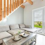 Wohnzimmer mit Sofa unter Treppe und Blick auf Feld durch Glastür