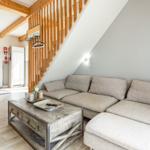 Wohnzimmer mit Sofa, Tisch und Holztreppe unter Dachschrägen.
