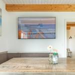 Esszimmer mit Holztisch, Sitzbank und Wandbildern. Fernseher an der Wand.