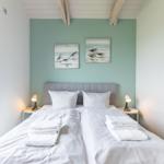 Schlafzimmer mit Bett, zwei Nachttischen und Fenster. Wand mit zwei Bildern.