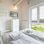 Schlafzimmer mit Bett, Kleiderständer und TV. Große Fenster mit Blick auf Grünfläche.