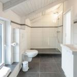 Badezimmer mit Dusche, WC und Waschbecken. Fenster mit Blick auf Balkon.