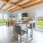 Küche mit Barhocker, Essbereich und Wohnzimmer mit Holzbalkendecke und Blick auf die Landschaft.