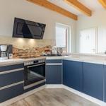 Küche mit blauen Schränken, Steinwand und Holzbalken an der Decke.