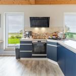 Küche mit blauen Schränken, Arbeitsplatte und Fenstern zum Garten.