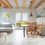 Wohn- und Essbereich mit Holzdecke, Sofa, Tisch und Stühlen sowie großen Fenstern.