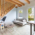 Wohnbereich mit Sofa, Tisch und Stühlen. Holzstufen und große Fenster.