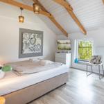 Schlafzimmer mit Bett, Fernseher und Fenstern zum Balkon