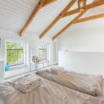 Schlafzimmer mit Doppelbett, TV und Balkonfenstern unter Holzbalkendecke.