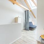 Schlafzimmer mit Dachschräge, Holzbalken und Fenster. Neben einem Bett steht ein Nachttisch mit Lampe.
