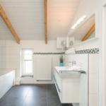 Badezimmer mit Dusche, Waschbecken und Fenster. Holzbalken an der Decke.