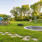 Grüner Garten mit Trampolin, Spielplatz und Steinweg.