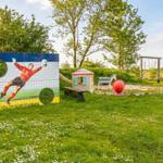 Spielplatz mit Tor, Sandkasten und Rutsche im grünen Garten.