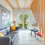 Wohnzimmer mit Sofa, Tisch und Stuhl, Holzstufen und Fenster zur Außenterrasse.