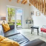 Wohnzimmer mit Sofa, roter Sitzgelegenheit und Terrassentür zum Garten.