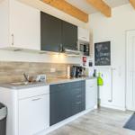 Küche mit weißen und grauen Schränken, Holzbalken an der Decke und einer Tür rechts.
