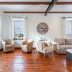 Living room with hardwood floor, sofa, armchairs, and wall clock.