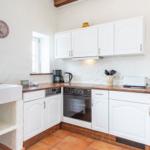Kitchen with white cabinets, wooden surfaces, and oven. Wall clock and window visible.