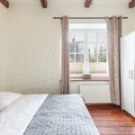Bedroom with bed, window, and wardrobe. Wooden floor and ceiling beams.