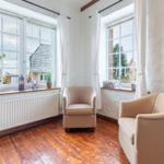 Two beige armchairs are in a room with hardwood floors and large windows.