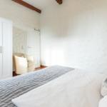 Bedroom with bed, wardrobe, and armchair. Ceiling with wooden beams.