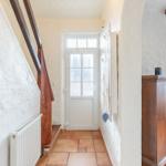 Entrance with wooden staircase, white door, and wooden cabinet. Terracotta floor and white walls.