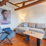 Living room with sofa, armchair, table, and wall art under wooden beams.