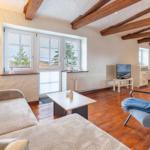 Living room with wooden beams, sofa, armchair, and TV. Wooden floor and windows with view.